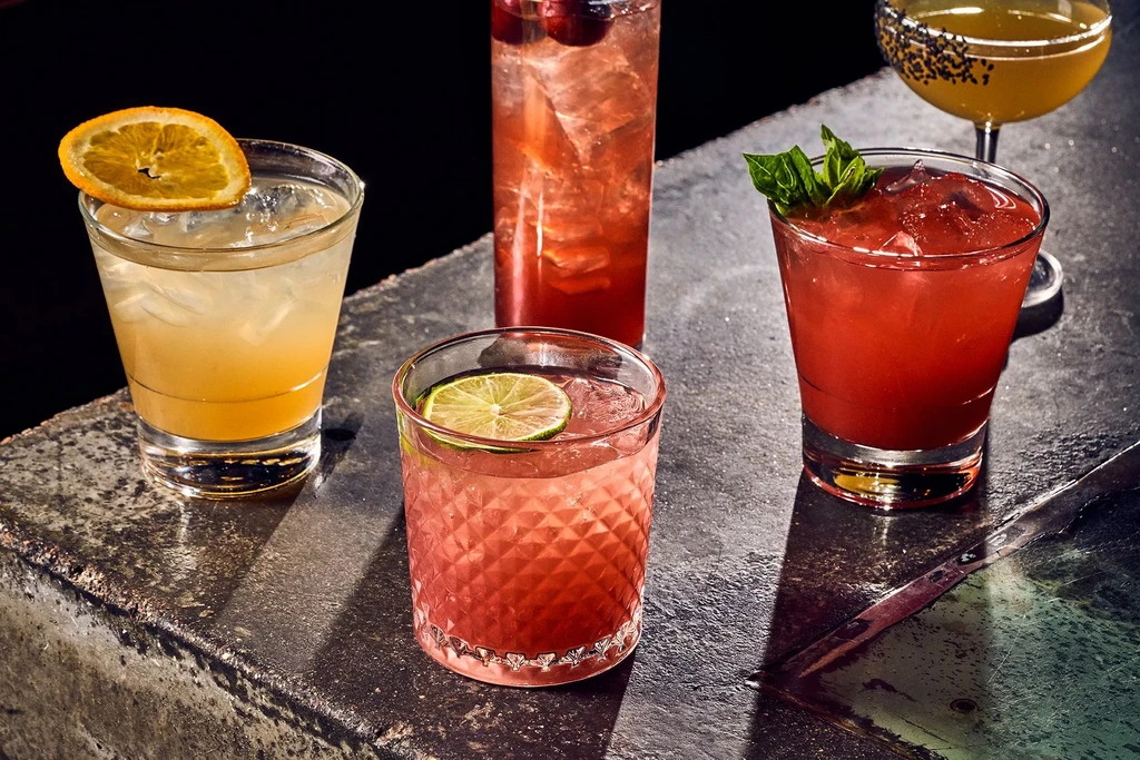 High-quality photo of five garnished cocktails on a dark bar top.