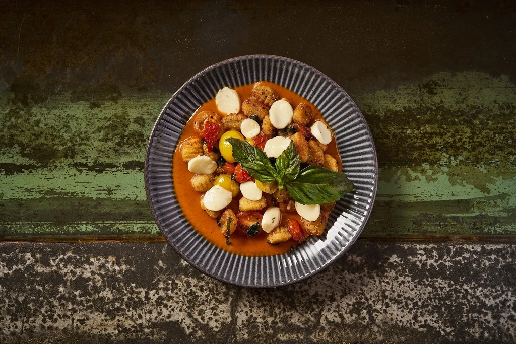 Gnocchi in tomato sauce with mozzarella, cherry tomatoes, and basil.