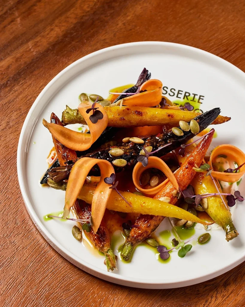 Roasted, glazed colorful carrots plated with seeds, microgreens, "Brasserie" dish.