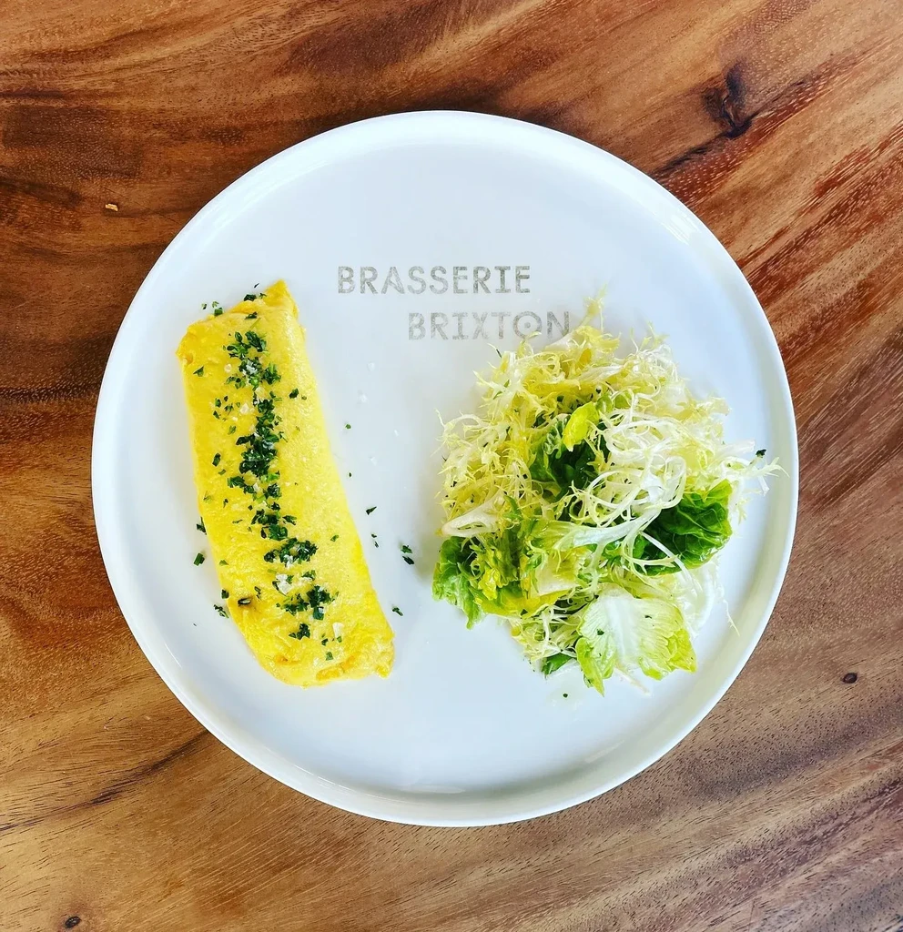 Golden rolled omelet with herbs, fresh salad, on Brasserie Brixton plate.