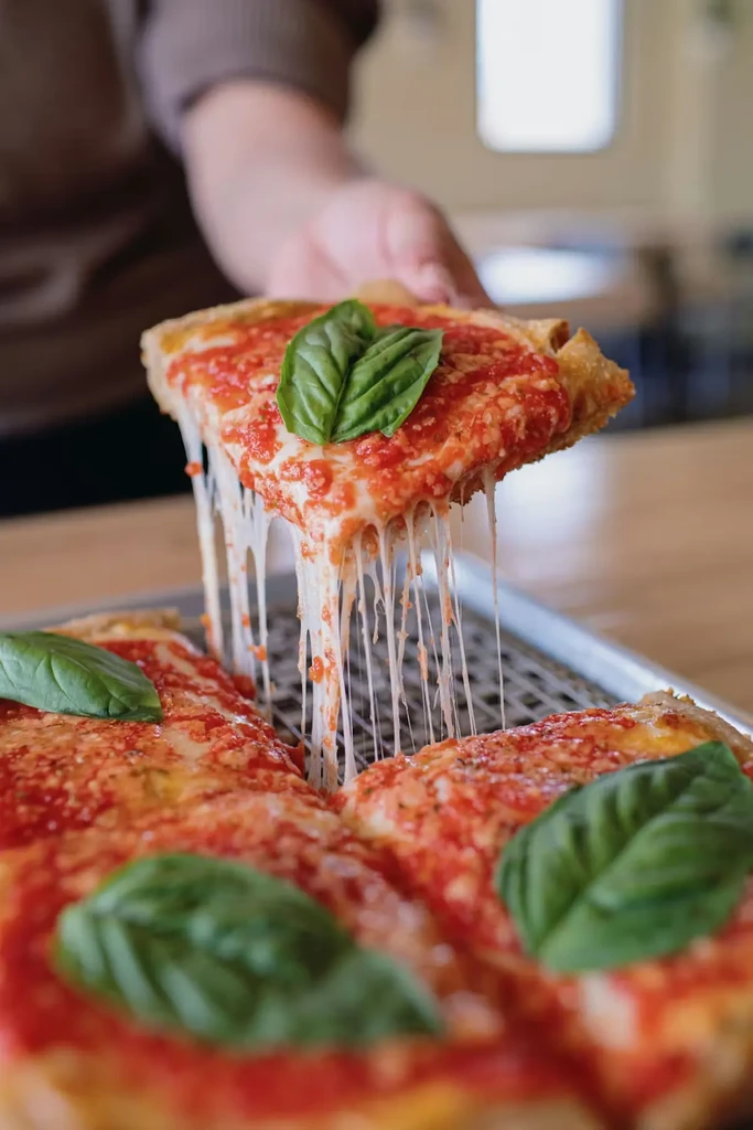 Hand lifts Margherita pizza slice, creating a long cheese pull.
