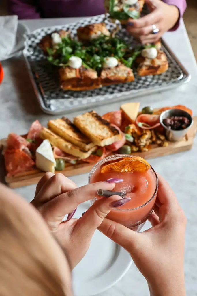 Hands hold a slushy drink, charcuterie board with meats and cheese.