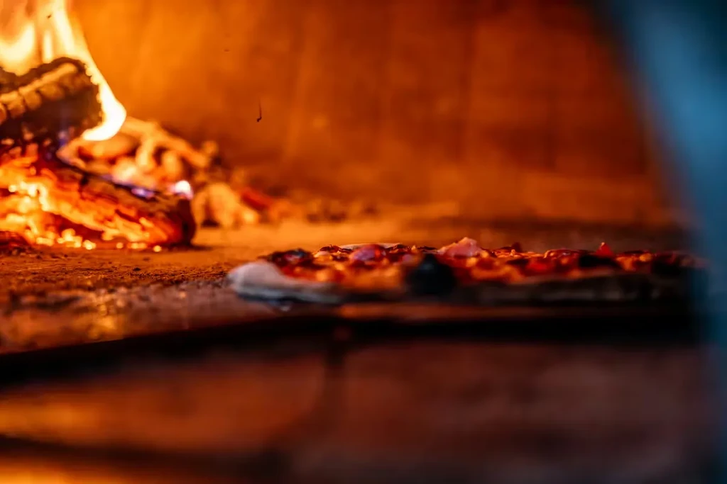 Pizza baking inside a wood-fired oven, lit by glowing embers.