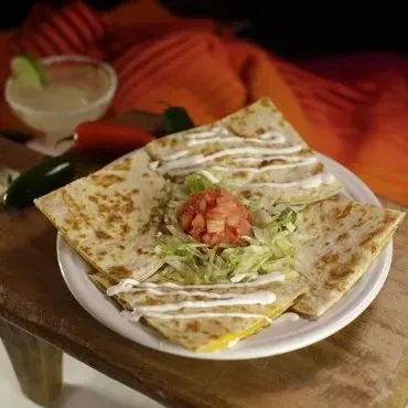 Plate of quesadillas, margarita, peppers on wood, with colorful textile background.