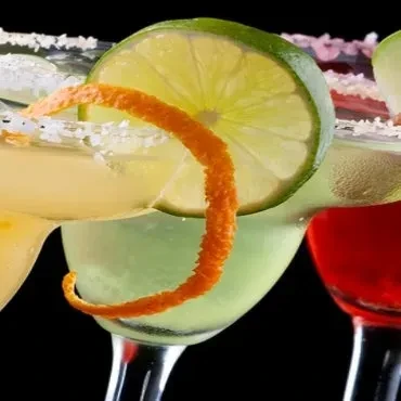 Three colorful cocktails with salt rims, garnishes, on a dark background.