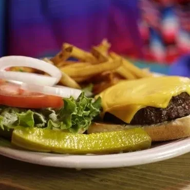 Cheeseburger, fries, pickle spear, lettuce, tomato, and onion on a plate.