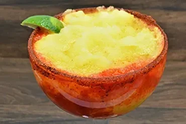 Frozen yellow drink in glass with chili-lime rim and lime wedge.