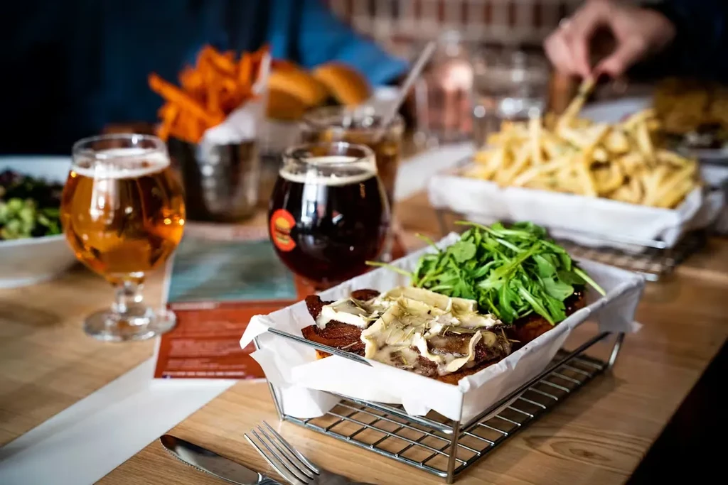 Burger with melted cheese, arugula, two beers, and fries on a table.