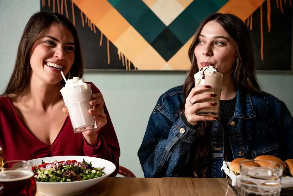 Young women drinking milkshakes and eating salad in a restaurant.