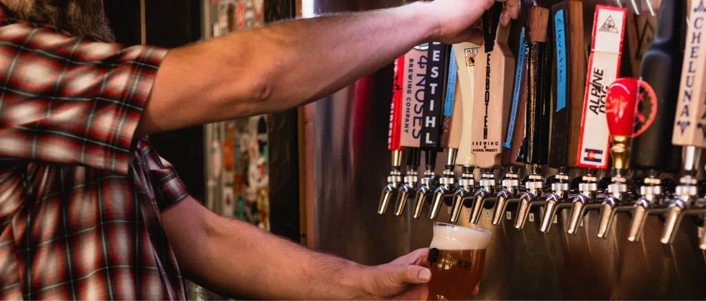 Person in plaid pouring beer from craft taps at a bar.