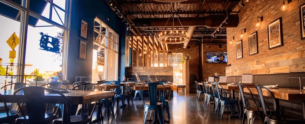 Modern, empty industrial-chic restaurant interior with large windows.