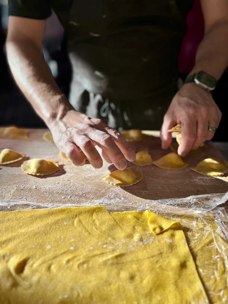 Person's hands shaping fresh pasta on a floured wooden board.