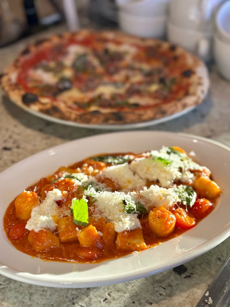 Gnocchi in red sauce with white cheese, basil, and blurred pizza.