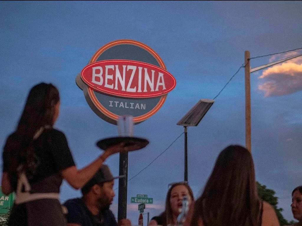 Bright BENZINA ITALIAN neon sign illuminates an outdoor evening dining scene.