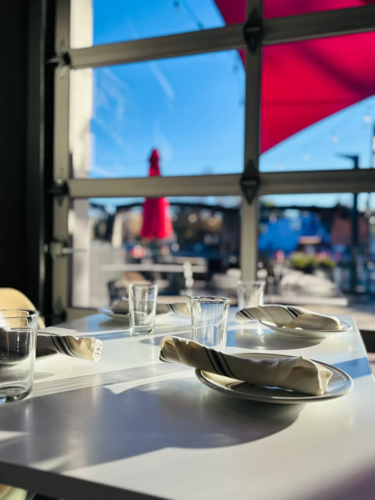 Sunlit restaurant interior, a table with four place settings, red umbrella.