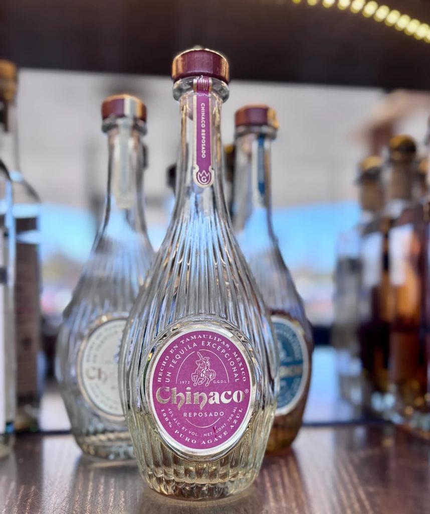 Purple-labeled Chinaco Reposado tequila bottle, ribbed glass, surrounded by others.