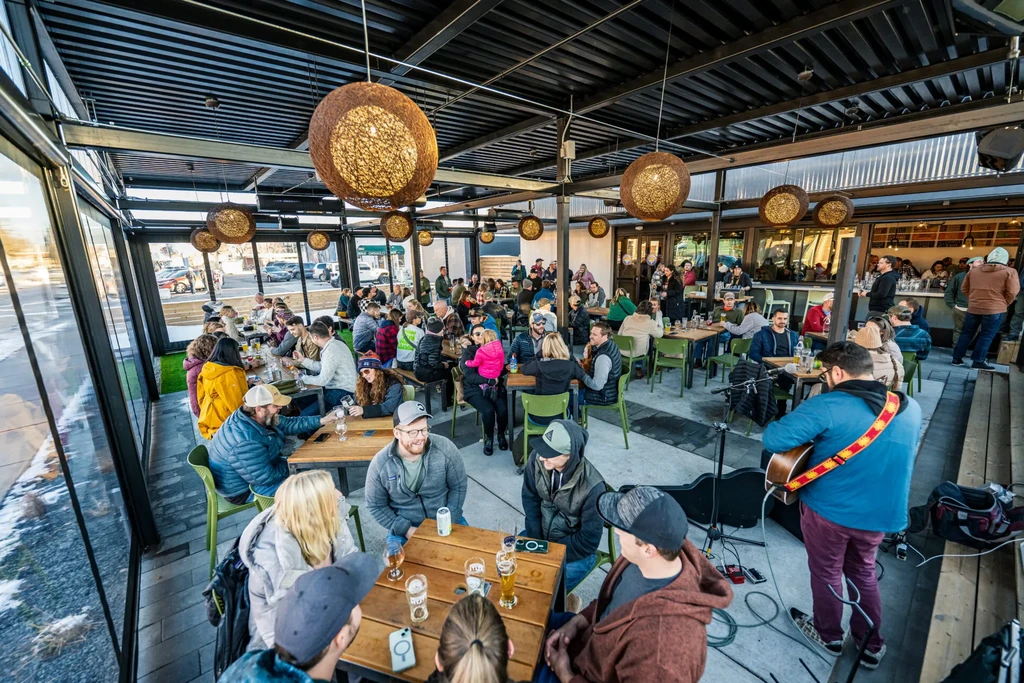 Lively indoor-outdoor brewery patio with people, live music, street view.