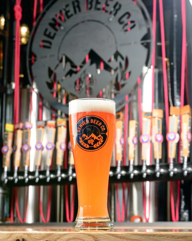 Denver Beer Co. amber beer with frothy head on wooden bar.