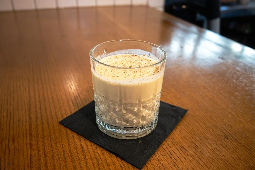 Creamy beverage in an embossed glass with spices on a wooden surface.
