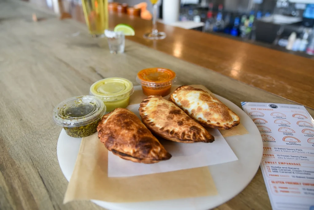 Three golden empanadas with three colorful sauces on a bar.