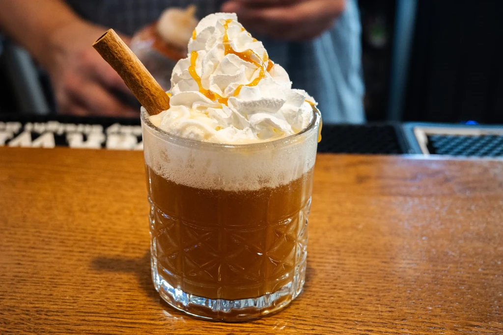 Brownish-orange drink with whipped cream, caramel drizzle, cinnamon stick.