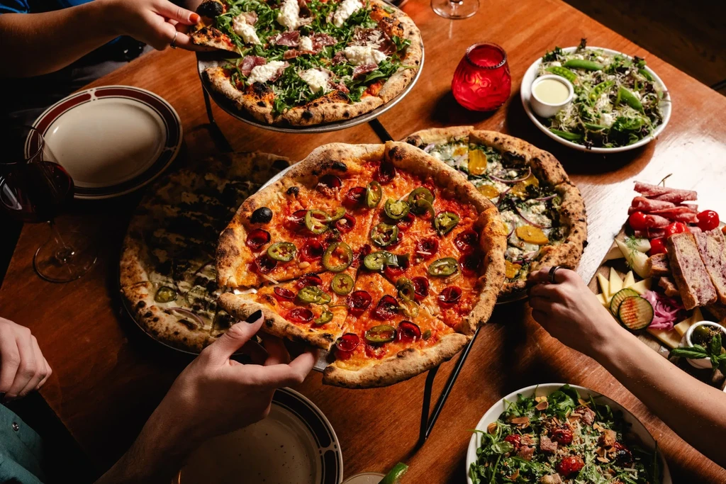 Overhead view of hands reaching for pizzas, salads, and charcuterie.