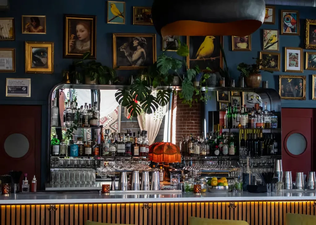 Stylish, well-stocked bar with gallery wall, plants, and vintage lamp.