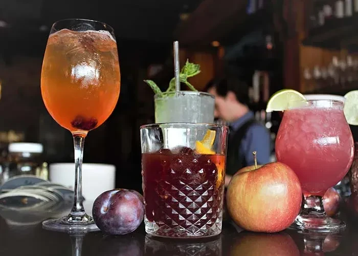 Several vibrant cocktails and fresh fruit on a dark bar counter.