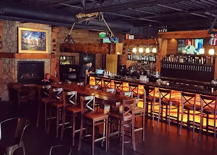 Rustic restaurant interior with fireplace, communal table, and glowing bar.