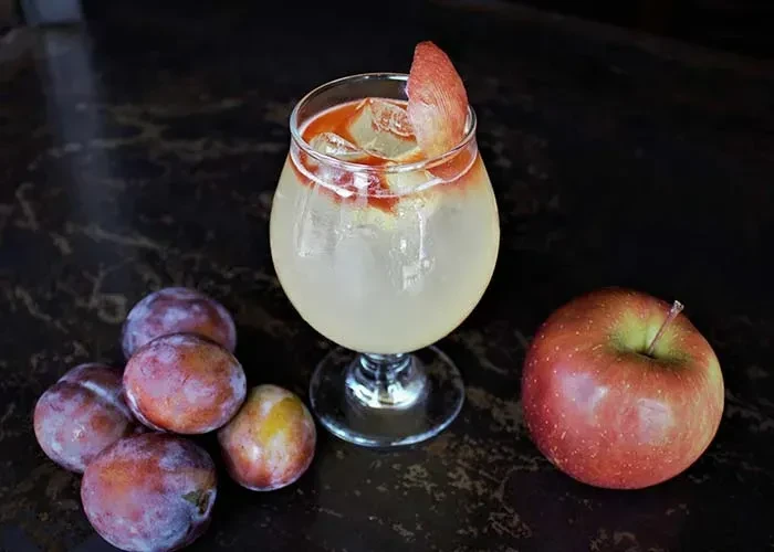 Cocktail in goblet with red drizzle, fruit, plums, and apple.