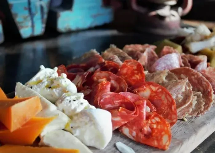 Charcuterie board with sliced meats, orange, and soft white cheeses.
