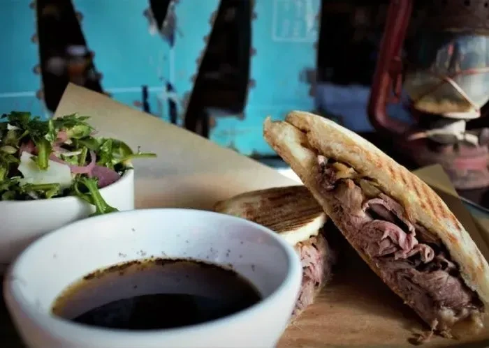 Grilled roast beef panini, green salad, and dipping sauce on a board.