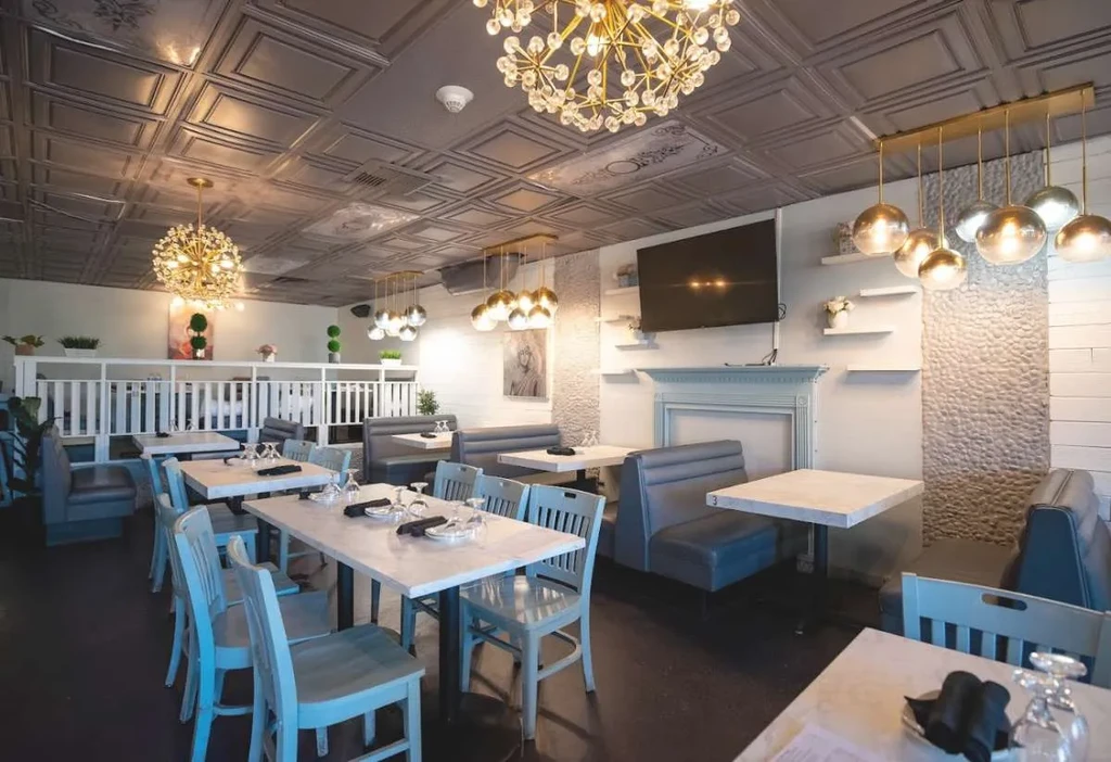 Restaurant interior features ornate ceiling, golden chandelier, blue chairs, and tables.