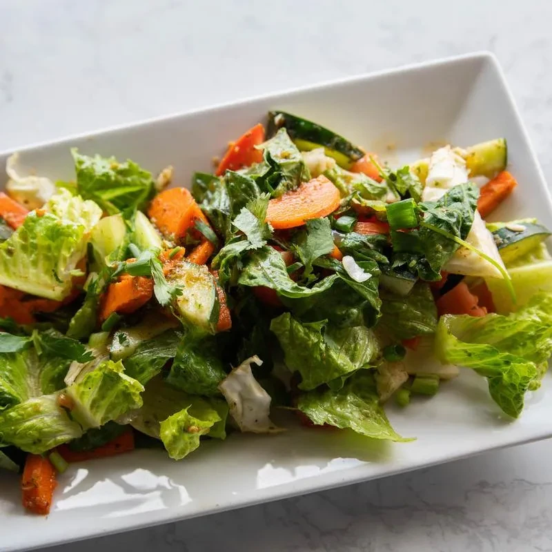 Fresh green salad with carrots and cucumber on a white plate.