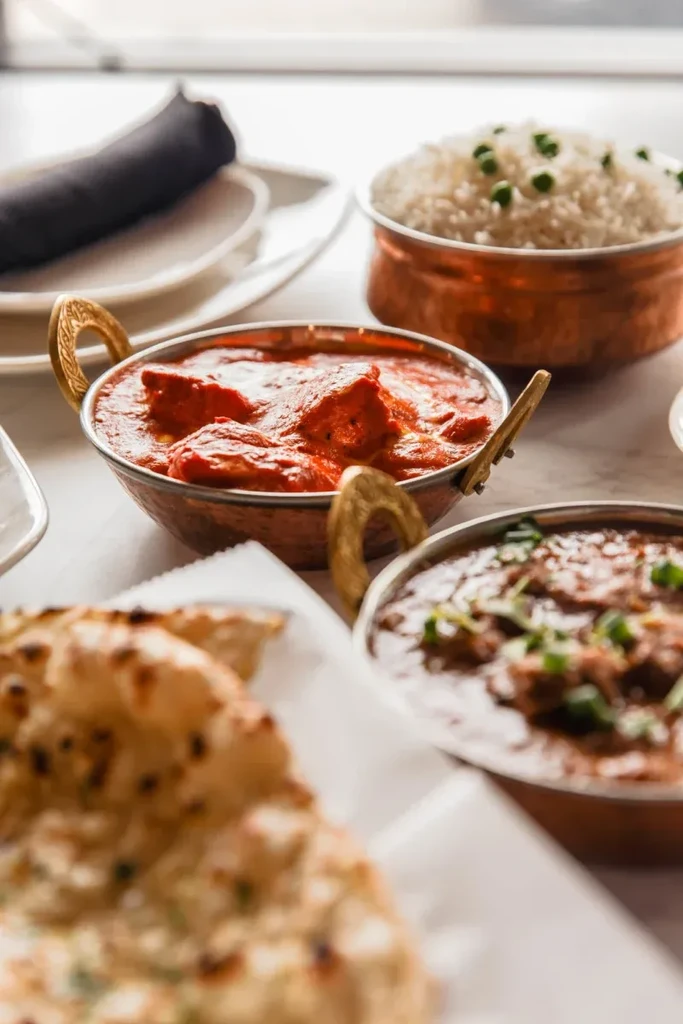 Tabletop with three copper bowls of Indian curries, rice, and naan.