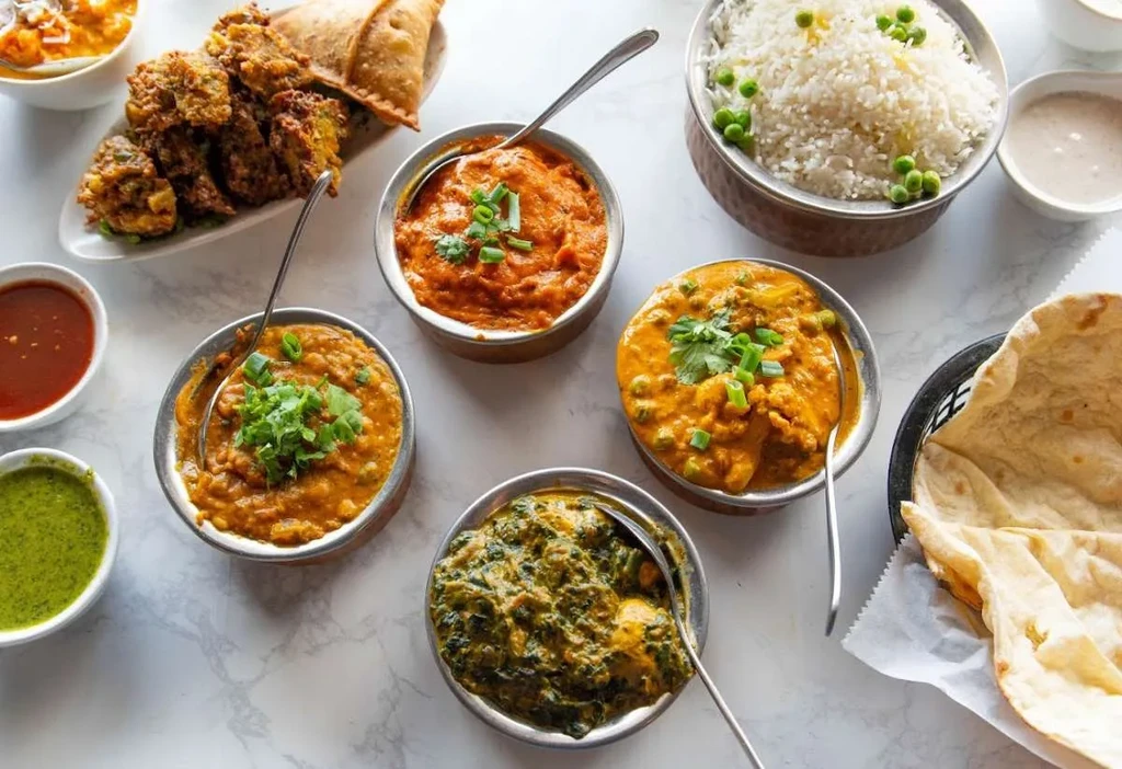 Overhead shot of Indian curries, rice, naan, and appetizers on a tabletop.