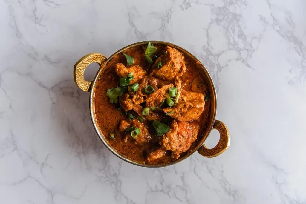 Reddish-brown curry in an ornate brass bowl, garnished with green herbs.