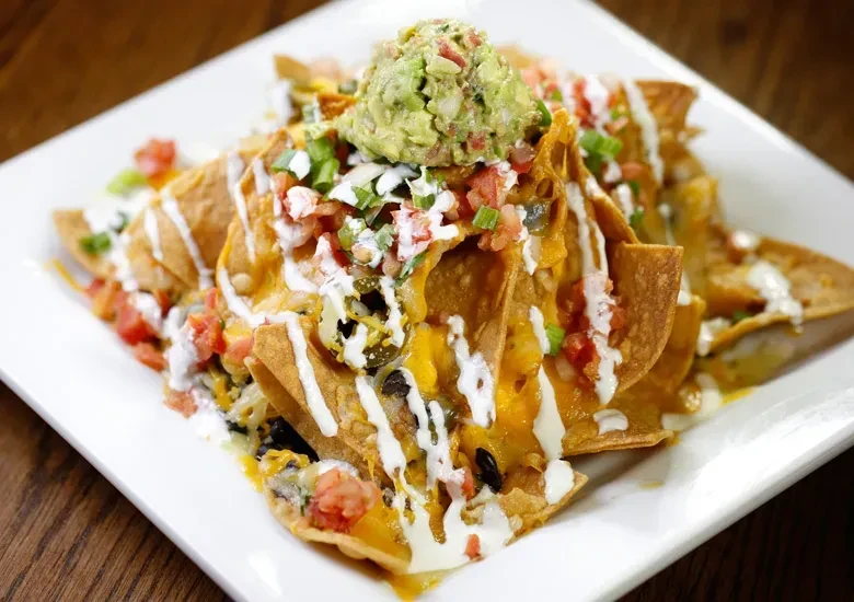 Nachos piled with melted cheese, guacamole, sour cream, beans, and jalapeños.