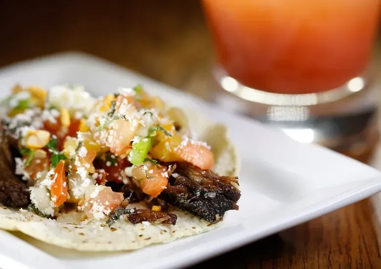 Single soft taco with shredded meat, salsa, and cheese on white plate.