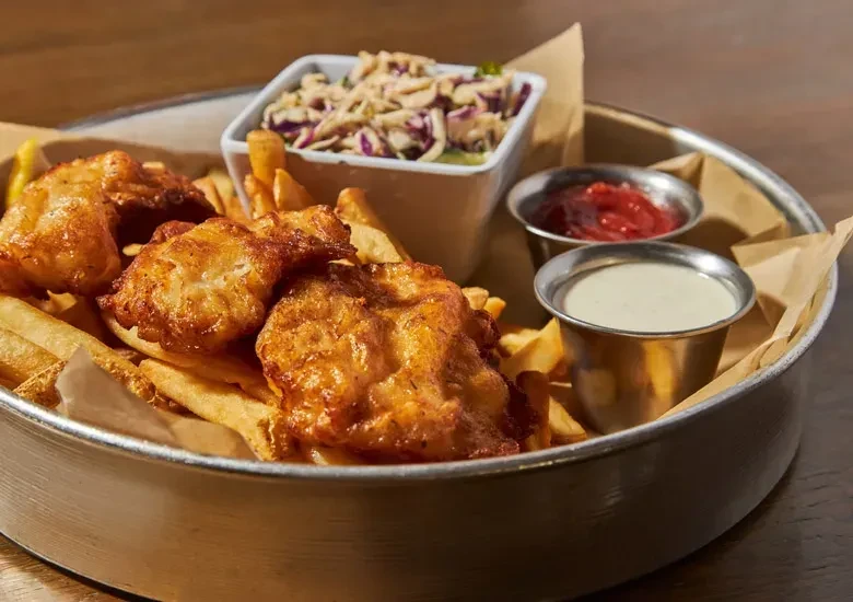 Fried fish and french fries meal with coleslaw and sauces.