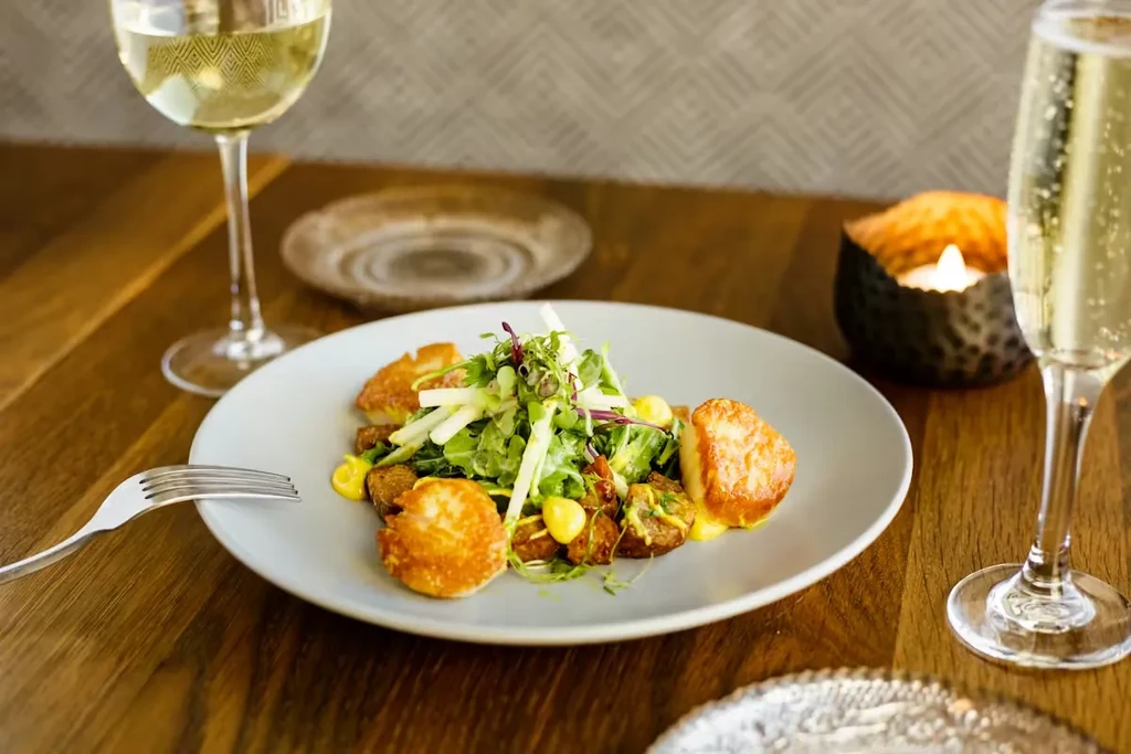 Close-up: plated salad with scallops, wine, and champagne on wood table.