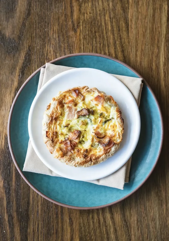 Savory quiche with bacon and vegetables on nested plates and wood.