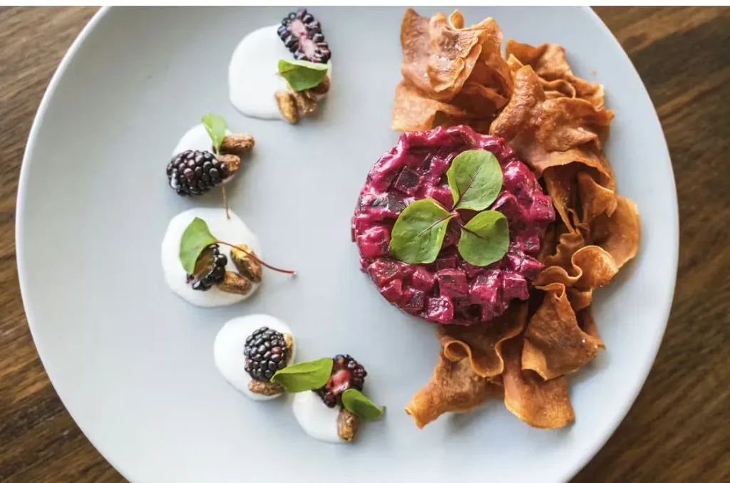 Plated red vegetable tartare, sweet potato chips, creamy sauce, blackberries.