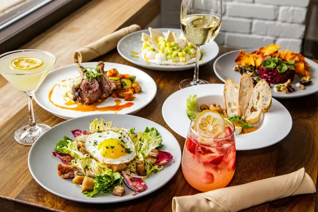 Five distinct plates of food and three drinks on a wooden table.