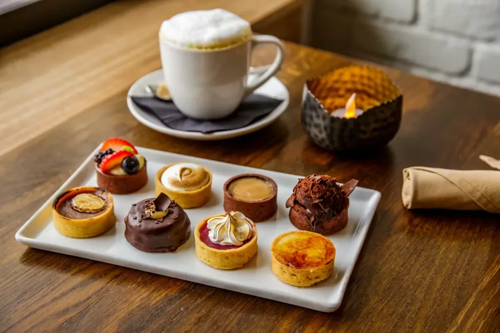 Platter of eight miniature tarts with coffee on a wooden table.