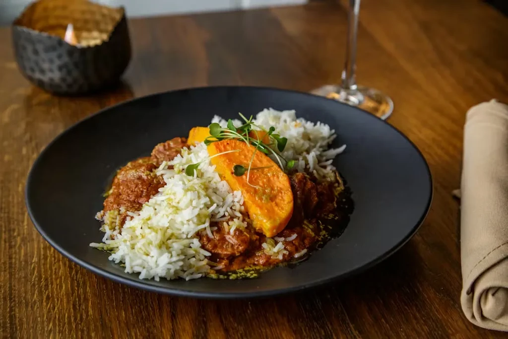 Reddish-brown stew topped with rice, orange vegetable, and microgreens.