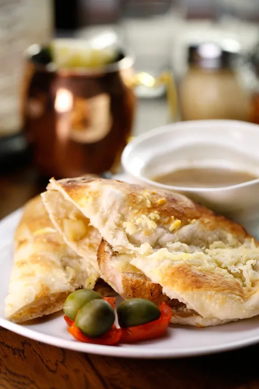 Close-up of baked flatbread with melted cheese, olives, and bell pepper.