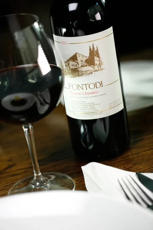 Red wine glass and Le Fontodi Chianti Classico bottle, dining table setting.