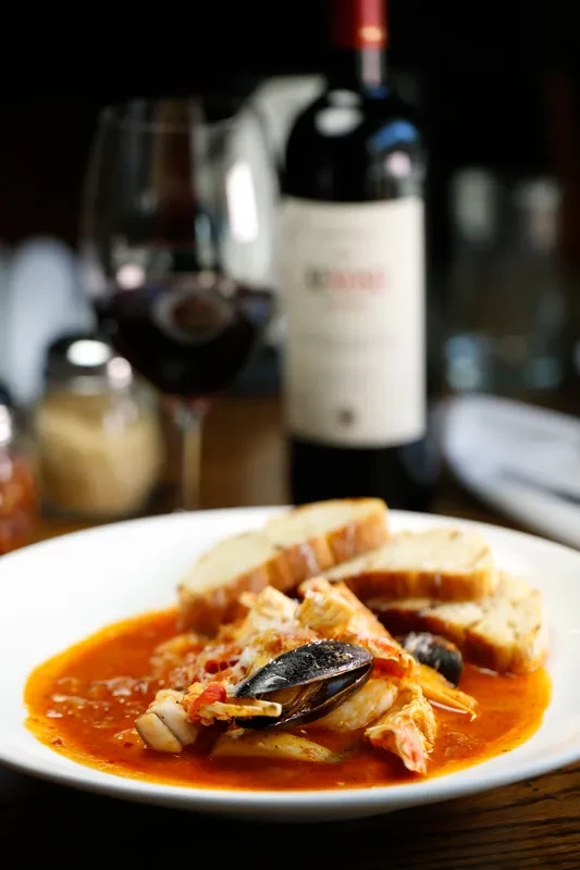 Reddish-orange seafood stew with mussels, shrimp, and toasted bread slices.
