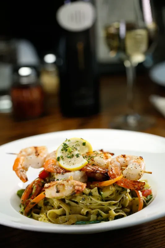 Close-up of pesto pasta with grilled shrimp, vegetables, and lemon.